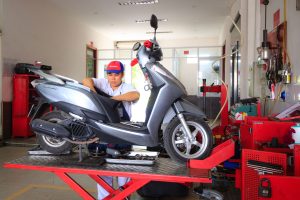 Mechanic working on a scooter in a well-equipped workshop, showcasing maintenance and repair services.
